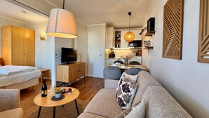 A modern living room with a sofa, a TV, a dining table, and a kitchen area. - Stilvolle Ferienwohnung mit Balkon in Sellin (Sellin)