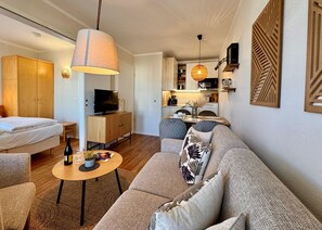 Ein modernes Wohnzimmer mit Sofa, Fernseher, Esstisch und Küchenzeile.