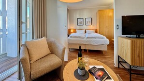 A hotel room with a bed, a television, a sofa, a wooden cabinet, and a window with curtains. - Stilvolle Ferienwohnung mit Balkon in Sellin (Sellin)