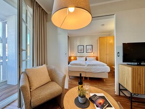 Ein Hotelzimmer mit Bett, Fernseher, Sofa, Holzschrank und einem Fenster mit Vorhängen.