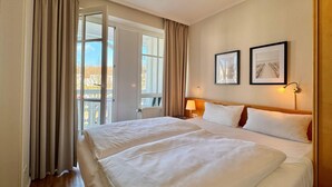 A hotel room with a large bed, a window with curtains, a wall-mounted lamp, and two framed pictures. - Stilvolle Ferienwohnung mit Balkon in Sellin (Sellin)