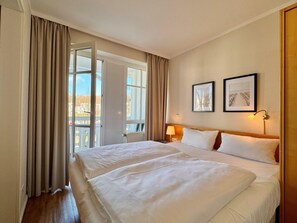 Ein Hotelzimmer mit einem großen Bett, einem Fenster mit Vorhängen, einer Wandlampe und zwei gerahmten Bildern.