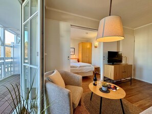Une chambre d’hôtel avec un balcon, un lit, une télévision, une armoire en bois et une table ronde avec une lampe.