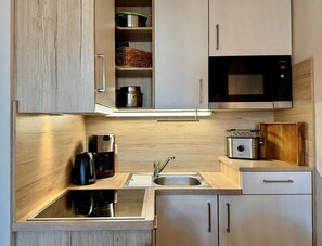 Une cuisine moderne dotée d’un four à micro-ondes encastré, d’appareils électroménagers en acier inoxydable et de meubles de rangement en bois.