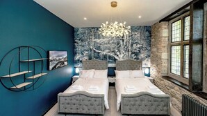 Une chambre avec deux lits, un lustre, une fresque murale et un mur en pierre.