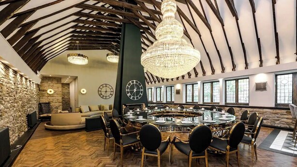 Une pièce spacieuse avec une grande table ronde, de nombreuses chaises, un mur en pierre et un plafond en bois.