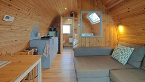 Interior acogedor de una cabaña con detalles de madera, una kitchenette, comedor y sala de estar con sofá y ventana.