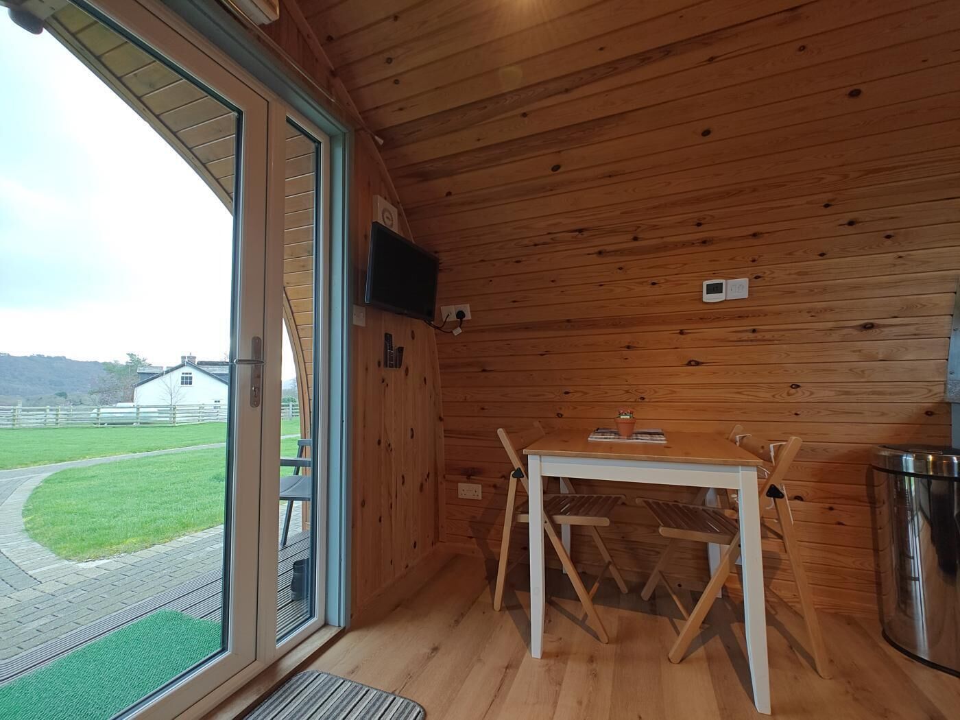 A wooden cabin with a table and chairs, a television, and a view of a grassy field.