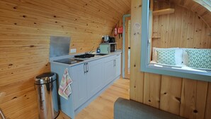 Cocina compacta con estufa, microondas y pileta, paredes de madera y ventana con vista.