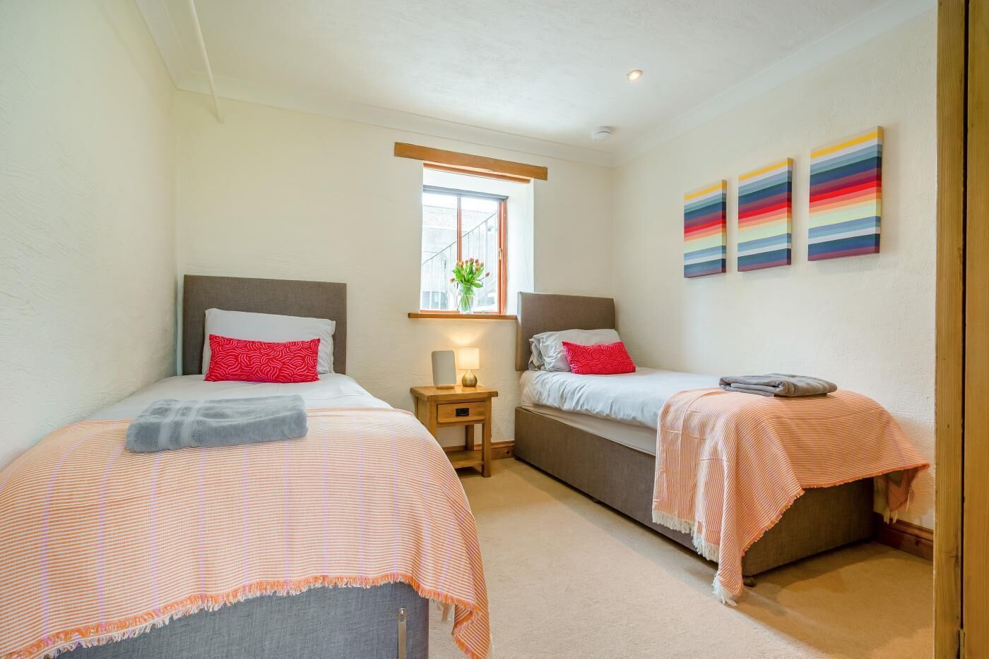 A bedroom with two beds, a window, a nightstand, and a wall with artwork.