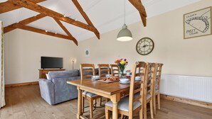 A dining area with a wooden table, chairs, a TV, and a clock on the wall. - 2 Bed in St. Ervan (oc-l36910) (Saint Ervan)