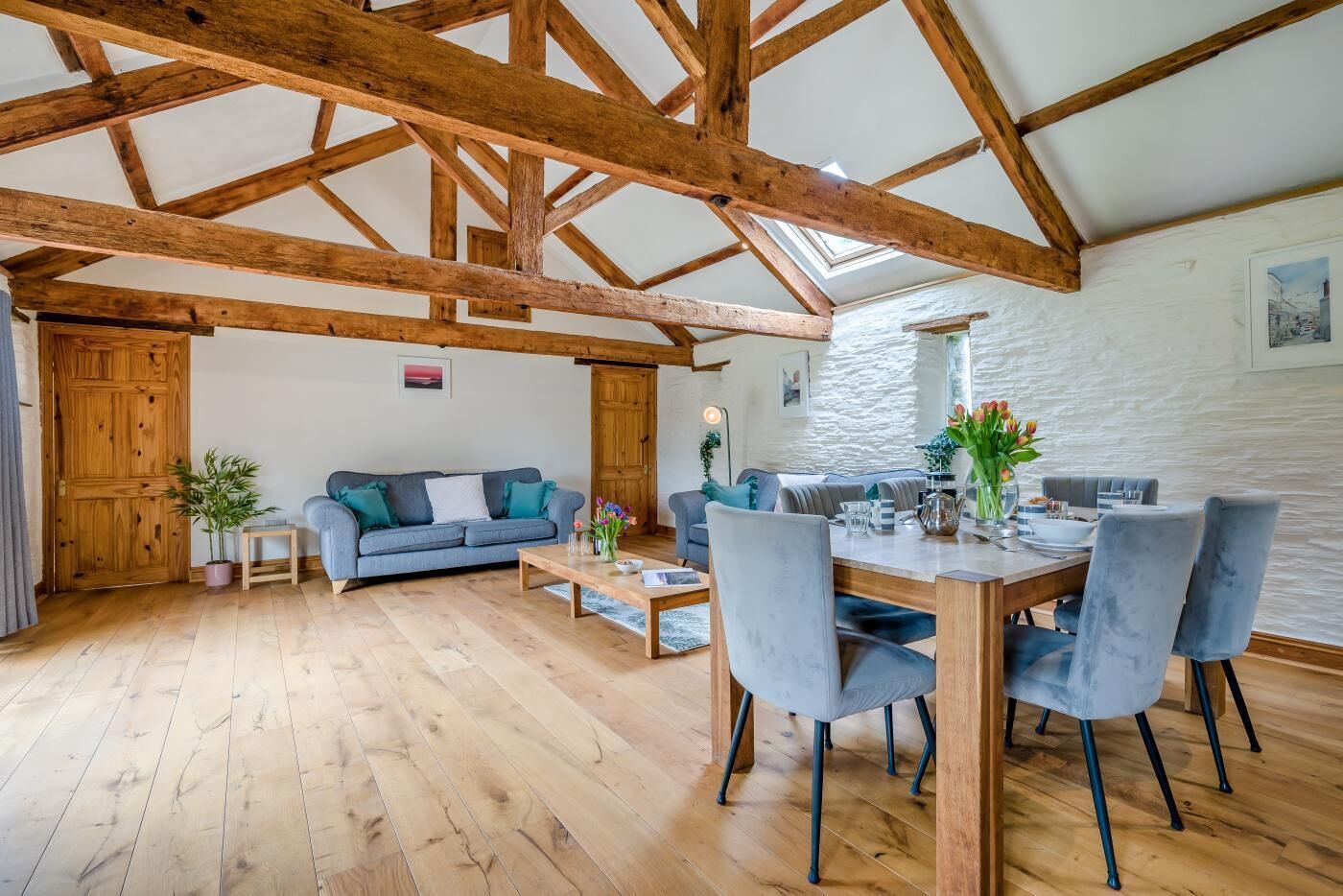 A spacious living area with a high wooden ceiling, a dining table with chairs, a sofa, and a small side table with a plant.