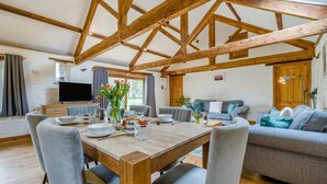 Een ruime woonkamer met een houten plafond, een eettafel voor vier personen en een grijze bank.