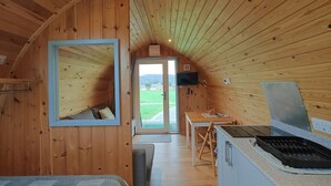 A cozy cabin interior with a wooden ceiling, a bed, a small kitchen area, and a view of the outdoors. - 1 Bed in Tyn-y-Groes (oc-g36301) (Ty'n-y-groes)