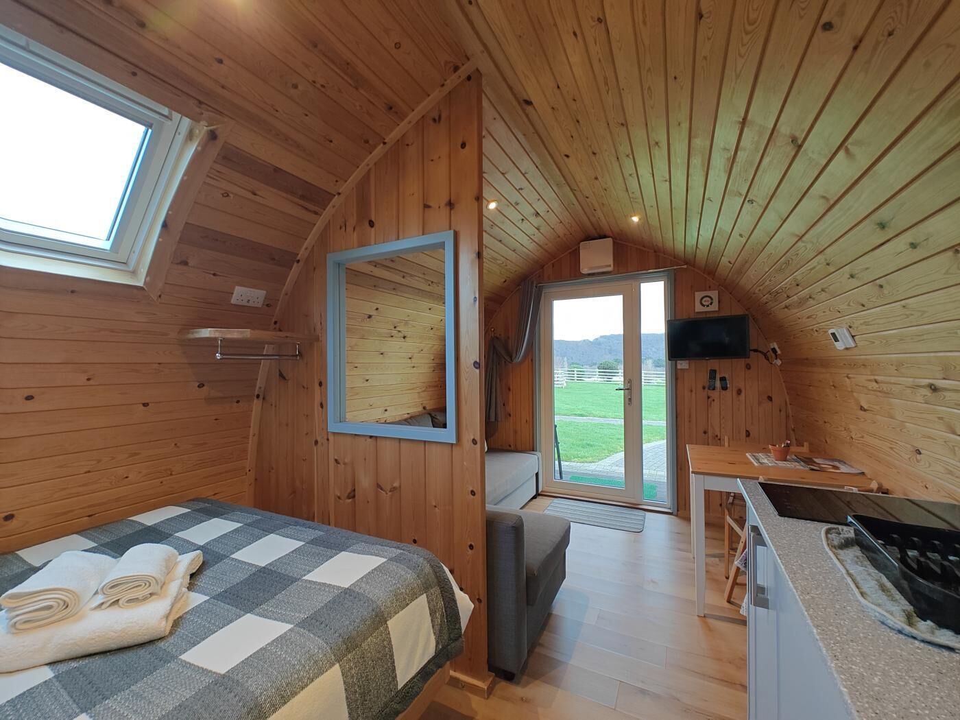 A cozy cabin with a bed, a small kitchenette, a mirror, and a door leading to a balcony.