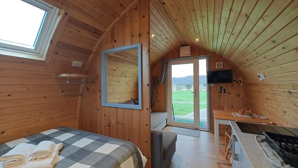 A cozy cabin with a bed, a small kitchenette, a mirror, and a door leading to a balcony. - 1 Bed in Tyn-y-Groes (oc-g36301) (Ty'n-y-groes)