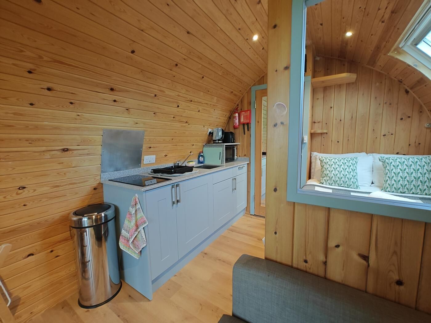 Une cuisine compacte équipée d’une cuisinière, d’un four à micro-ondes et d’un évier, avec des murs en bois et une fenêtre offrant une vue agréable.