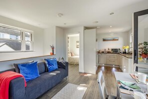 Ein modernes Wohnzimmer mit Sofa, ein Essbereich mit Tisch und Stühlen, eine Küche mit Schränken und Geräten sowie ein Flur, der in einen weiteren Raum führt.