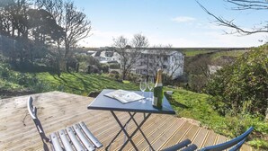 Une terrasse en bois avec une table, deux chaises, une bouteille de champagne et des verres.