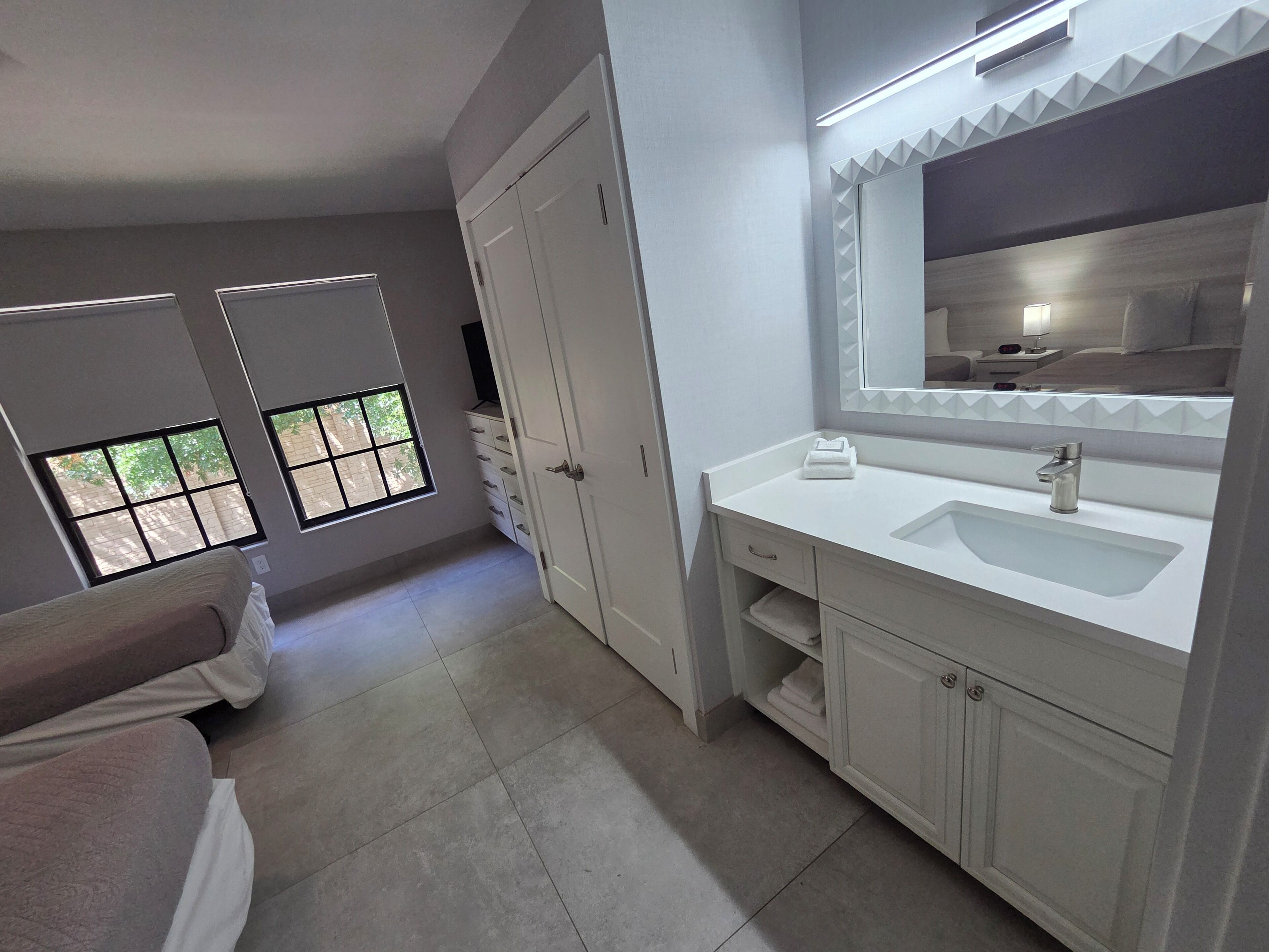 A modern bathroom with a large mirror, white vanity, and a window with a view.