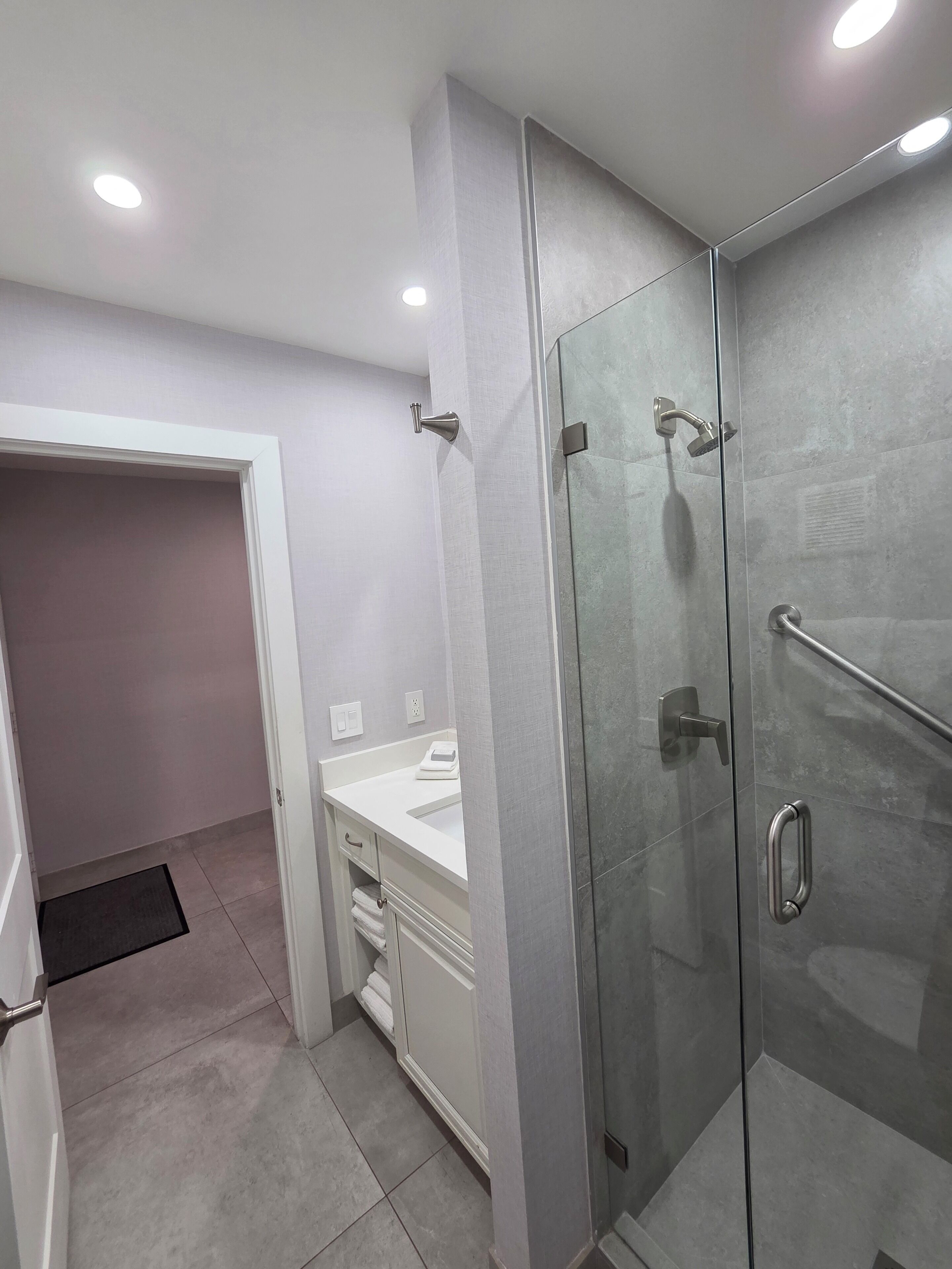 A modern bathroom with a glass shower enclosure, a white vanity, and a walk-in closet.