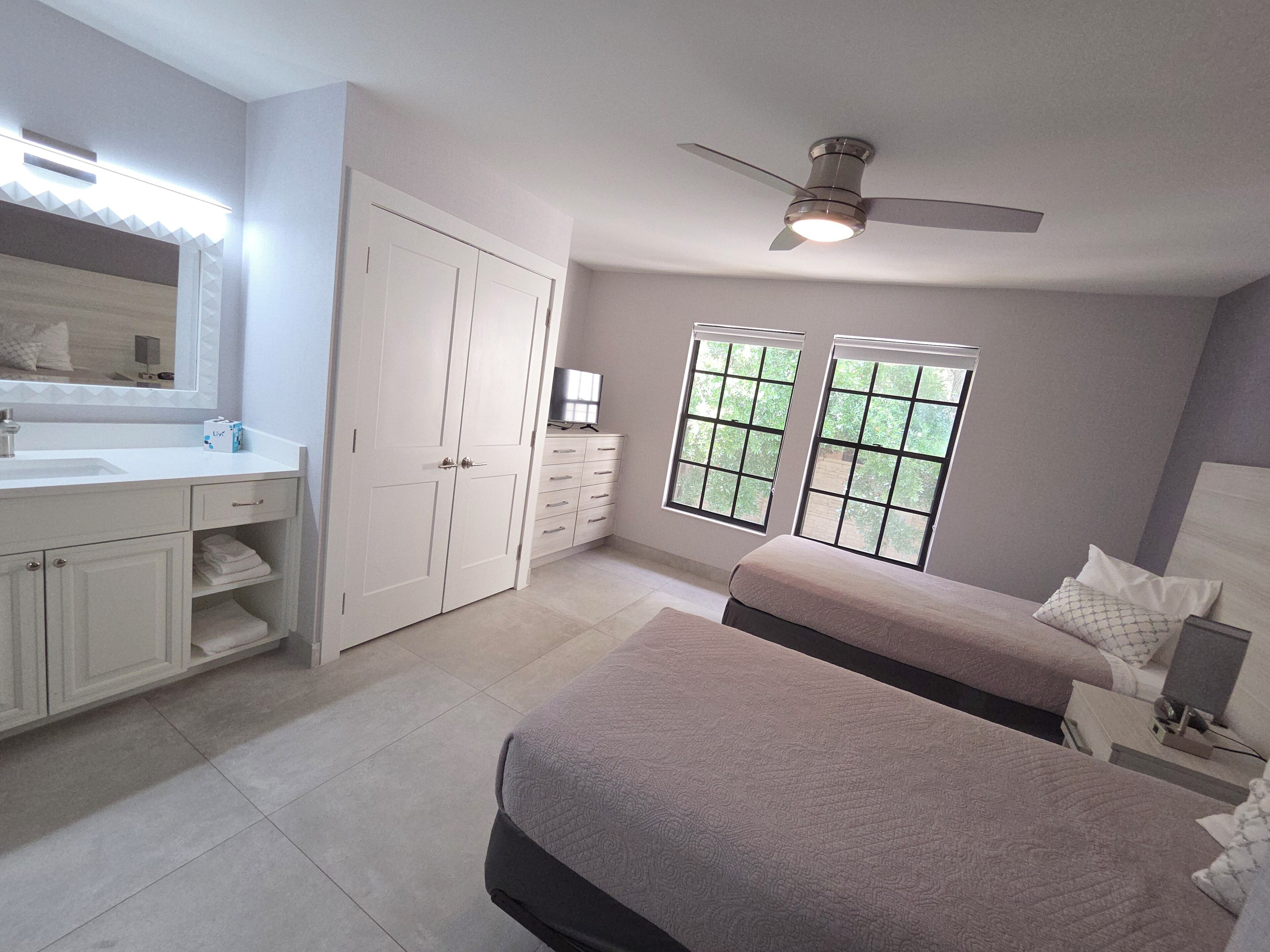 A bedroom with a bed, a dresser, a vanity, and a ceiling fan.