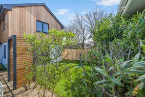 A modern house with a wooden exterior, a fenced backyard, and a variety of greenery. - 4 Bed in Padstow (oc-p36067) (Constantine Bay)