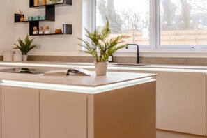 A modern kitchen with a central island, a window with a view of trees, and a sink. - 4 Bed in Padstow (oc-p36067) (Constantine Bay)