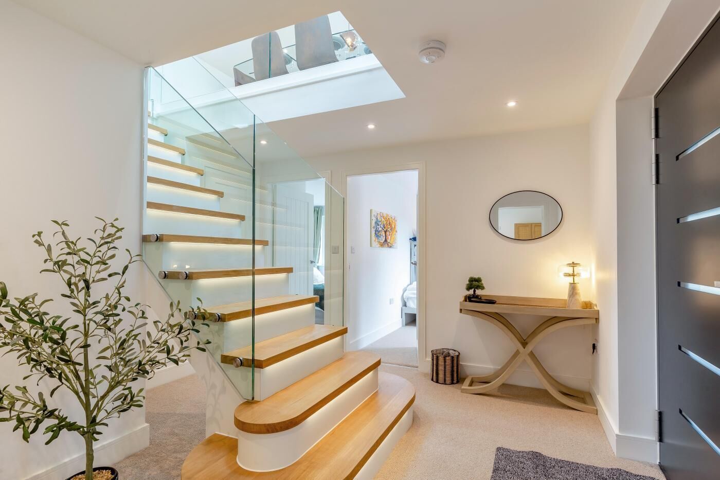 A modern interior with a glass staircase, a wooden console table, and a round mirror.