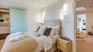 Ein modernes Schlafzimmer mit einem Bett, Nachttischen und einem durch eine geöffnete Tür einsehbaren Badezimmer.