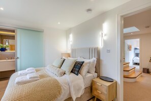Ein modernes Schlafzimmer mit einem Bett, Nachttischen und einem durch eine geöffnete Tür einsehbaren Badezimmer.