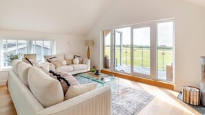 Ein geräumiges Wohnzimmer mit einer großen Couch, einem Glastisch und Blick auf eine grüne Landschaft durch große Schiebetüren.