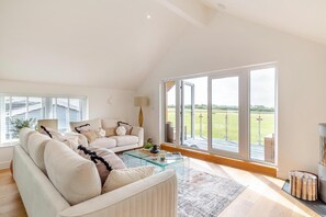 Ein geräumiges Wohnzimmer mit einer gro ßen Couch, einem Glastisch und Blick auf eine grüne Landschaft durch große Schiebetüren.