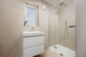 Ein modernes Badezimmer mit einer Glastrennwand-Dusche, einem weißen Waschbecken und einem Fenster mit einer Pflanze.