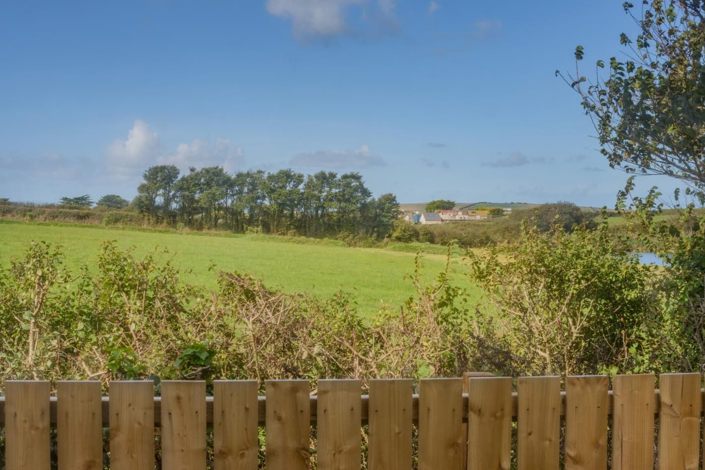 A wooden fence in the foreground with a view of a green field and trees in the background.