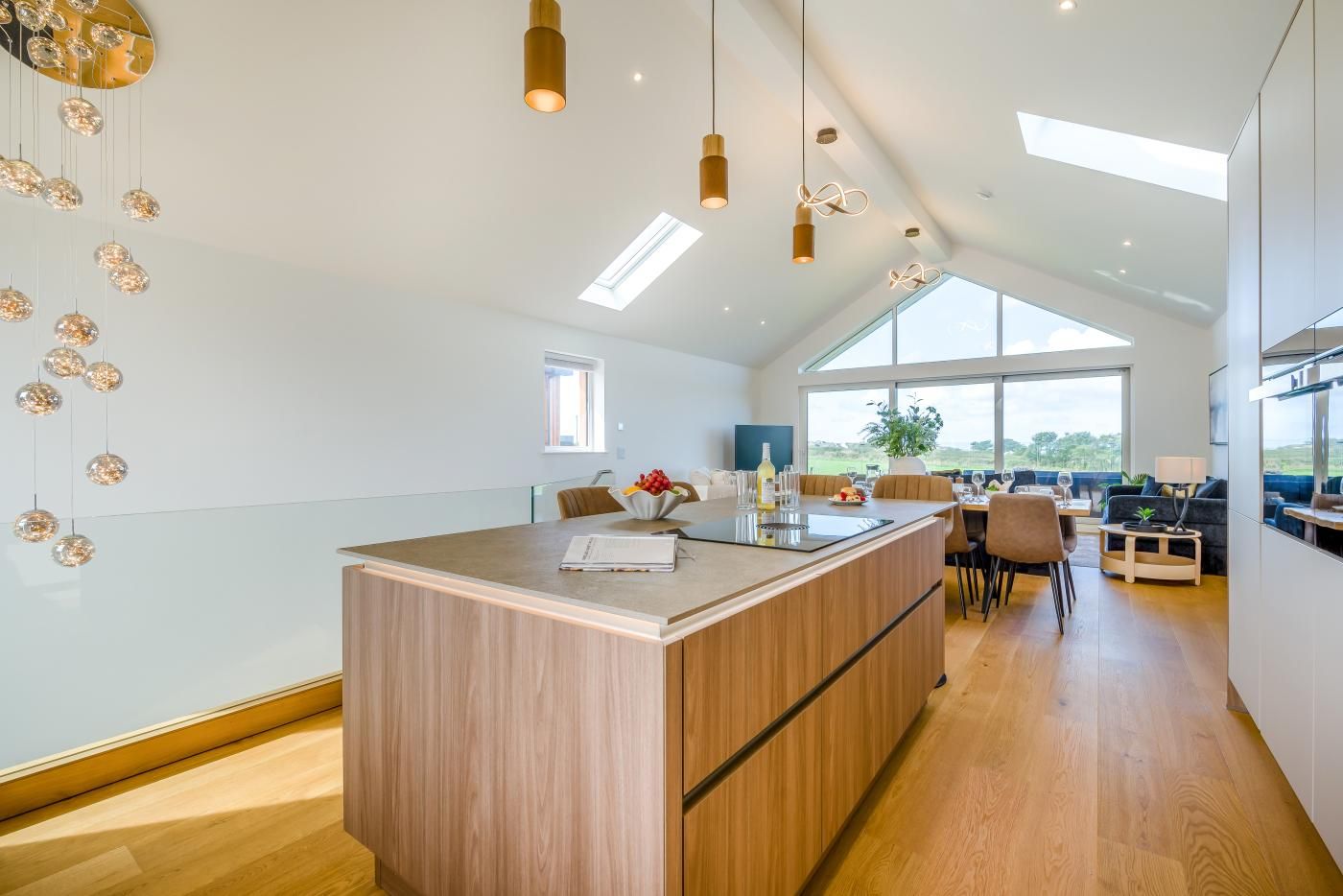 Een moderne keuken met een centraal eiland, hanglampen en grote ramen met uitzicht op de omgeving.