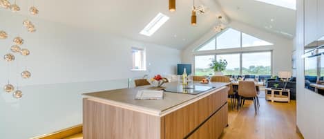 A modern kitchen with a central island, pendant lighting, and large windows offering a view of the outdoors.