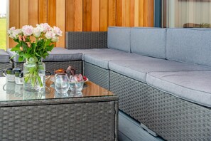 Ein moderner Außenbereich zum Sitzen mit einem Glastisch, Korbmöbeln und einem Blumenstrauß.