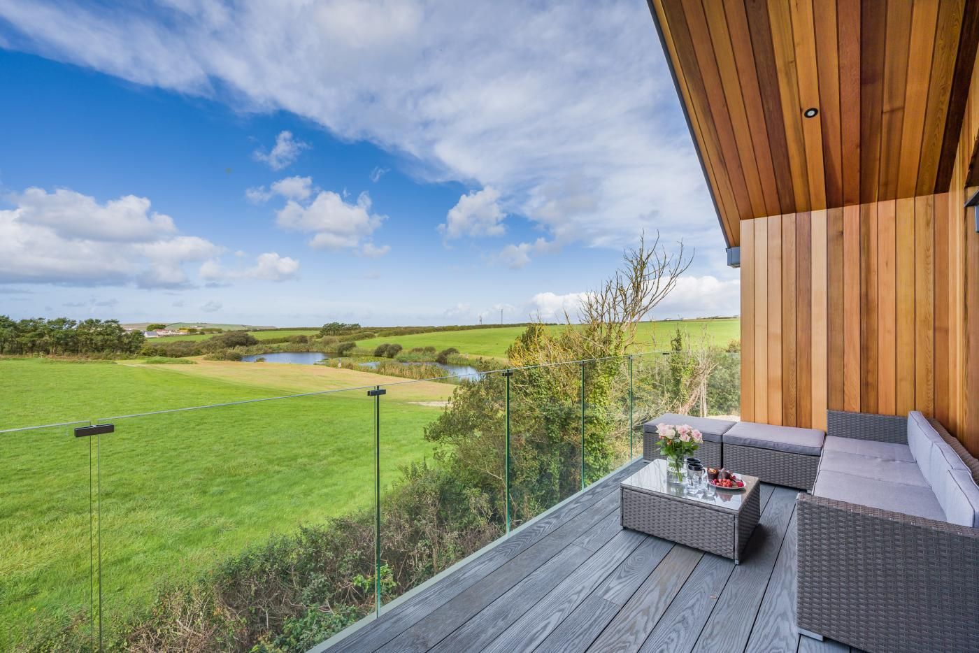 A wooden deck with outdoor furniture overlooking a green field and a body of water.