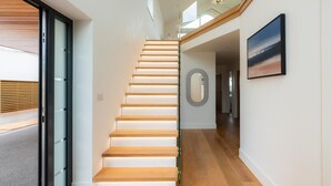 A modern interior with a staircase leading to a second floor, a glass railing, and a framed picture on the wall. - 4 Bed in Padstow (oc-p36070) (Constantine Bay)