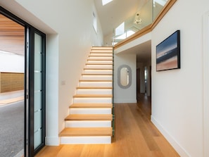 Ein modernes Interieur mit einer Treppe zu einer zweiten Etage, einem Glasgeländer und einem gerahmten Bild an der Wand.