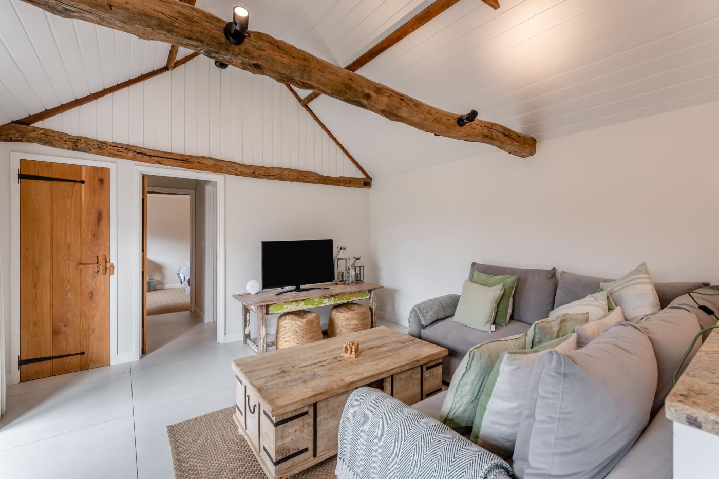 Un accogliente soggiorno con soffitto in legno, una zona divani, un tavolino da caffè e un televisore.
