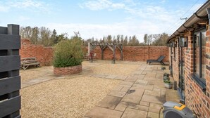 Une terrasse avec un mur en briques, une pergola en bois et un espace détente comprenant un banc et une chaise.