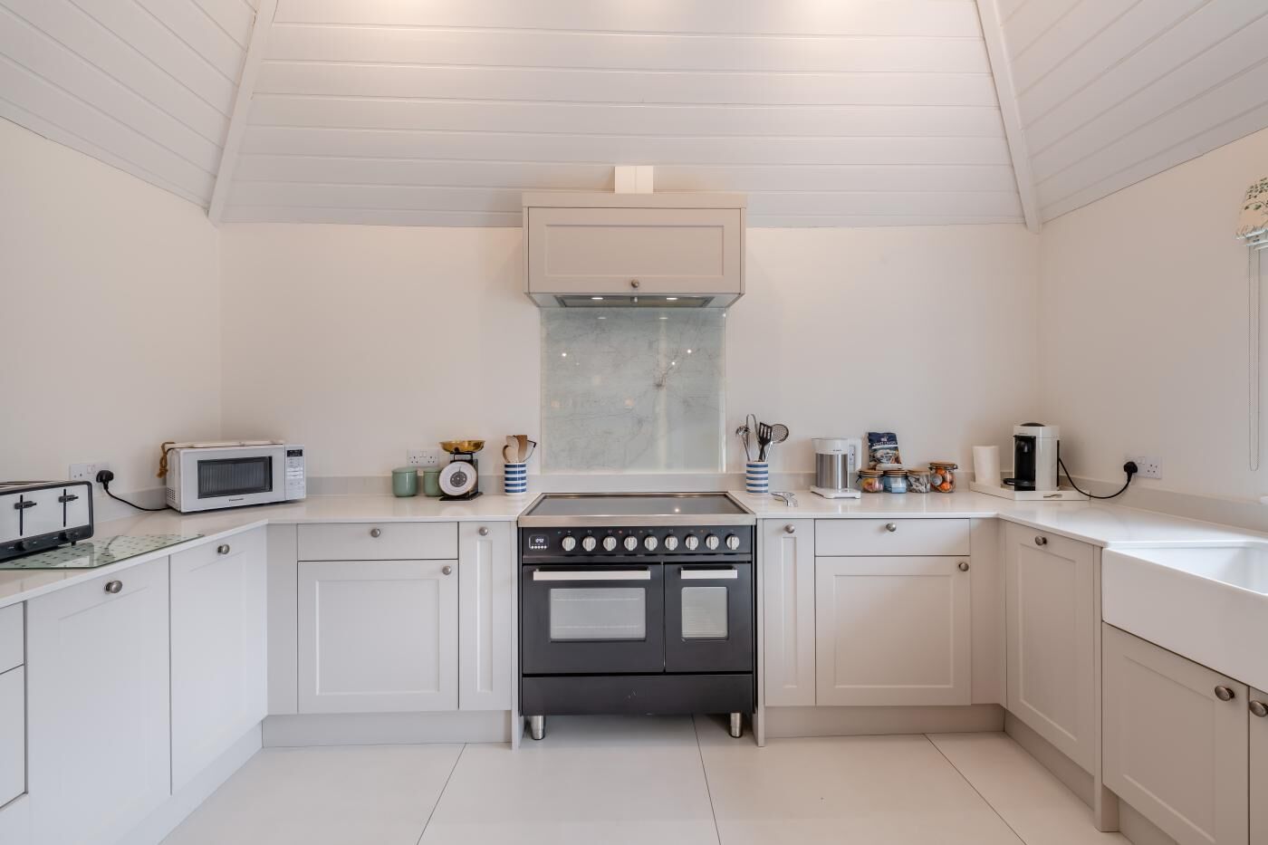 Una cucina moderna con mobili bianchi, forno integrato, microonde e macchina per il caffè.