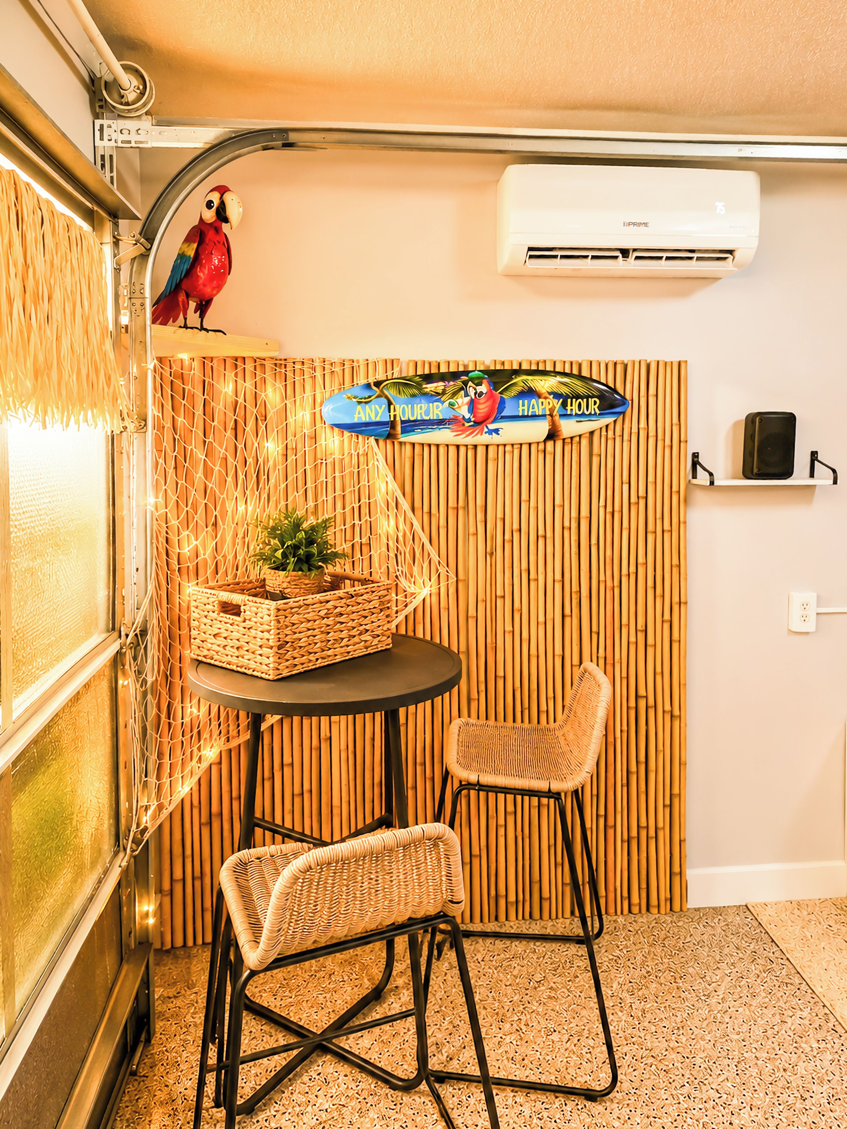 A compact room with a small table, two wicker chairs, a decorative wall with a 'Happy Hour' sign, and an air conditioning unit.