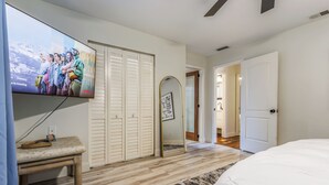 Een slaapkamer met een bed, een aan de muur bevestigde televisie, een bankje, een kledingkast en een spiegel.