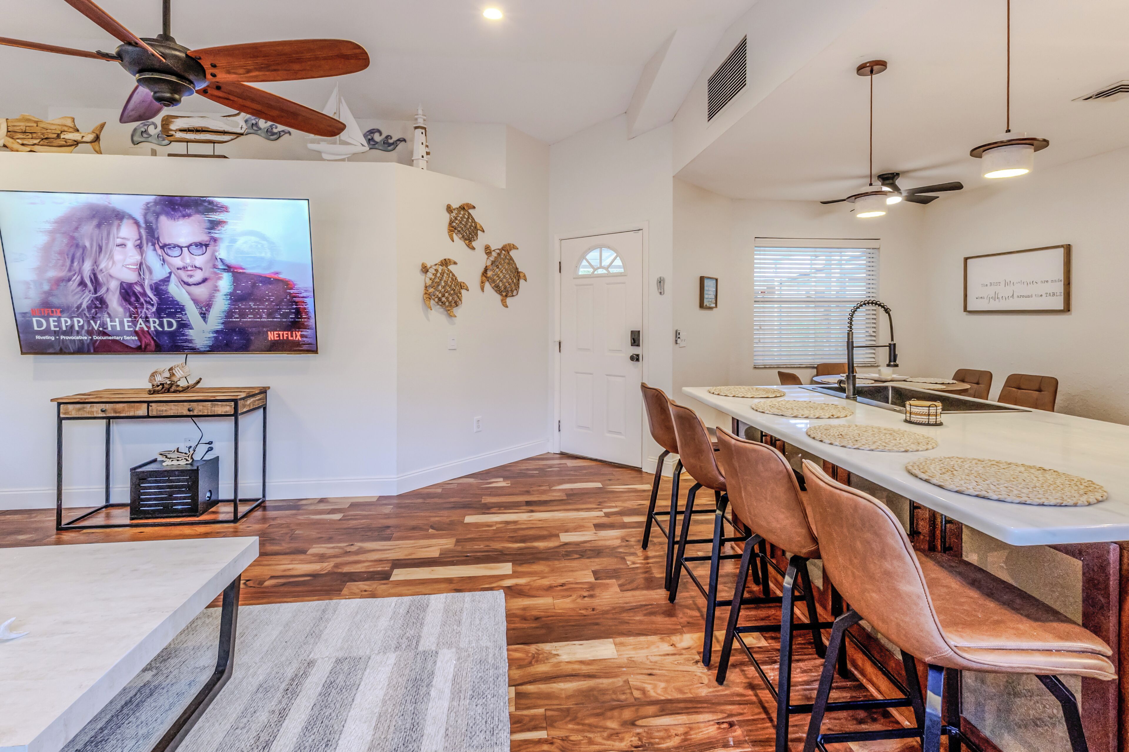 Una cocina moderna con zona de comedor, suelo de madera y un televisor mostrando 'DEPP v HEARD'.