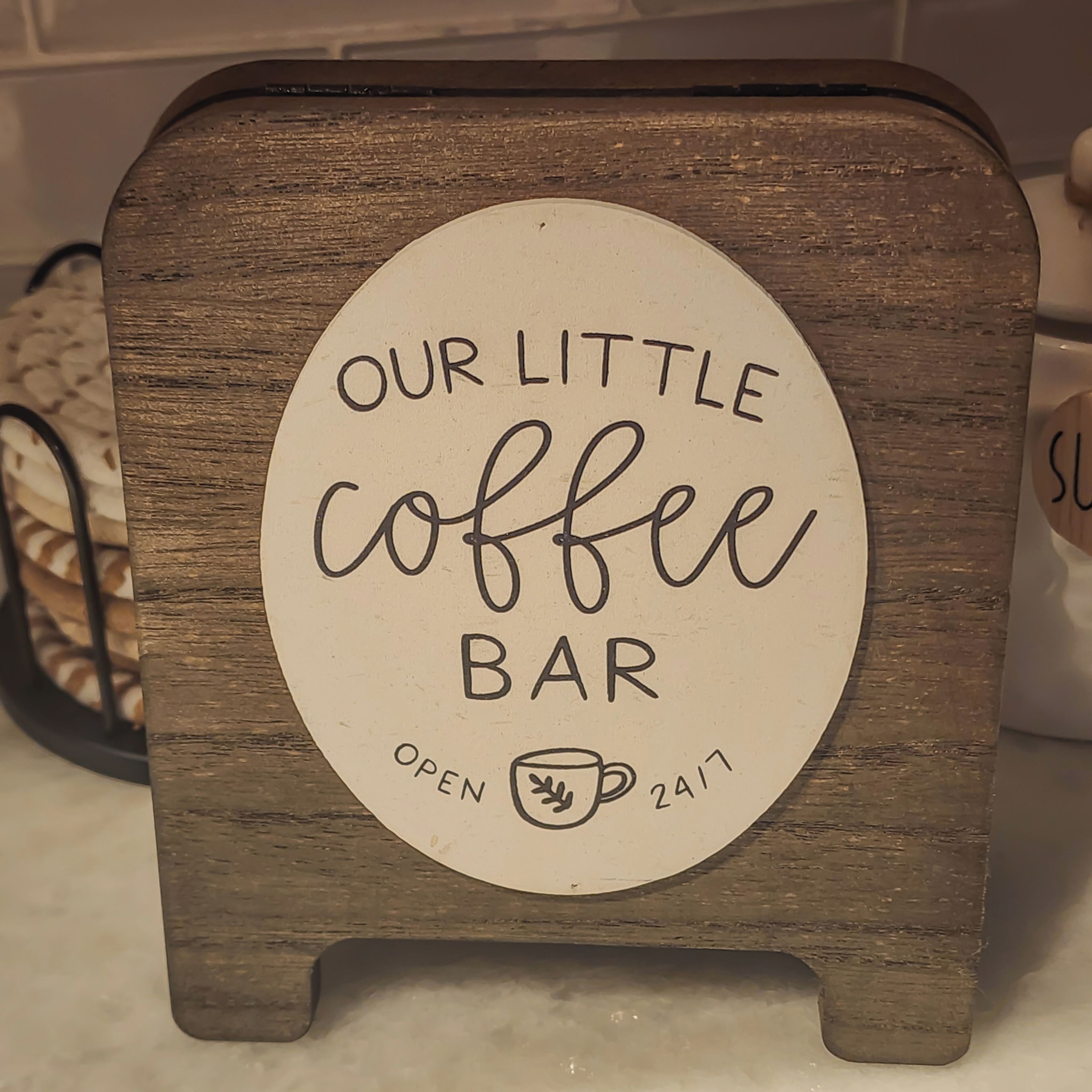Een houten bord waarop staat 'OUR LITTLE COFFEE BAR' en 'OPEN 24/7'.