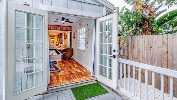 Een huis met een houten terras, een schuifdeur met glas, een plafondventilator en een klein vloerkleed.