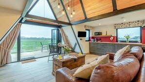 A modern interior with a dining area, a sofa, a kitchen, and a large window overlooking a field.